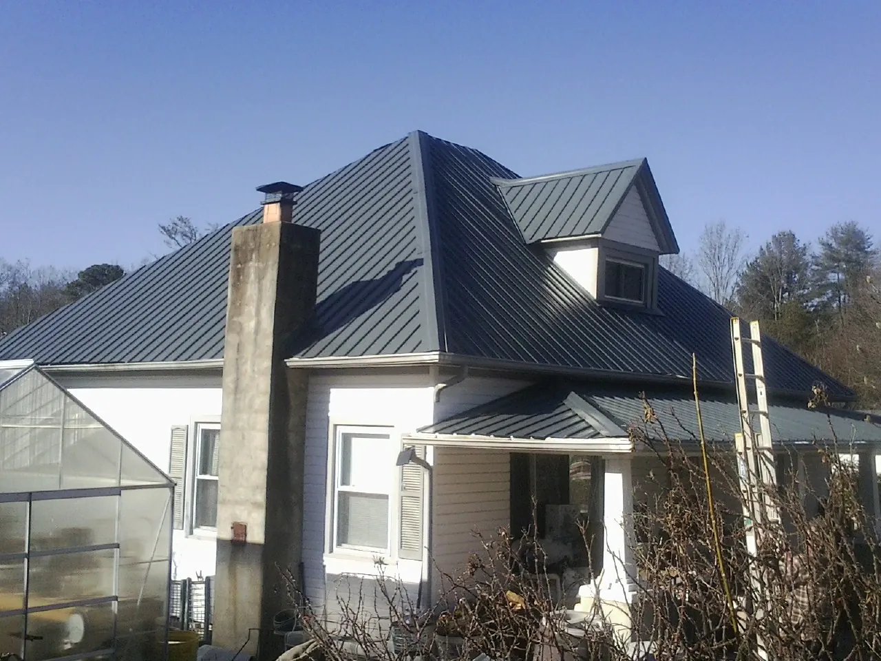Dark blue standing seam metal roof on a white farmhouse with dormer — Slate & Tile Roof Repair by Roofing Brothers in Poseyville