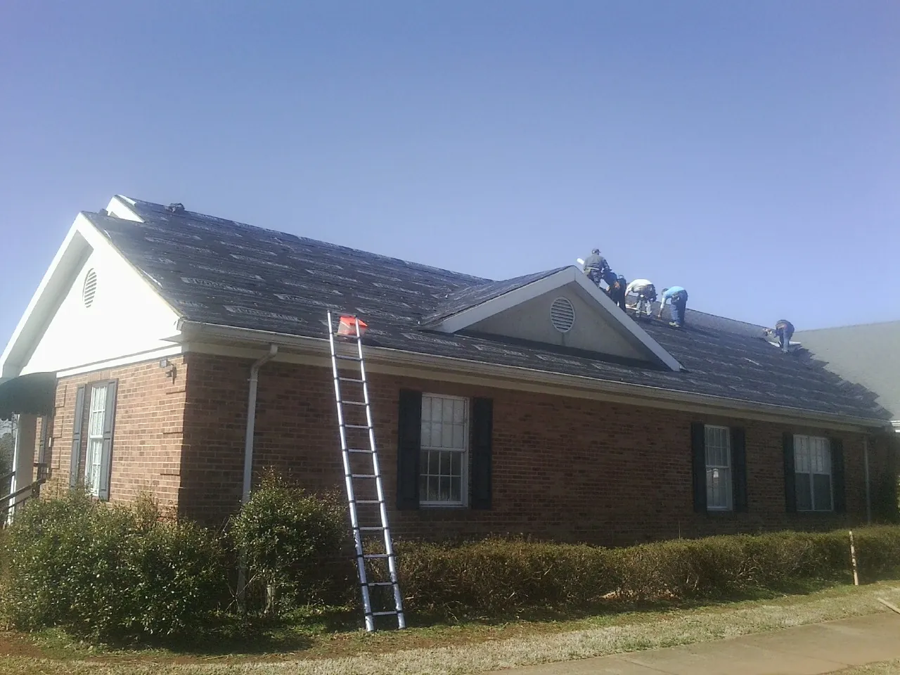 Crew tearing shingles off a brick ranch roof with a ladder set — Emergency Roof Repair work by our crew in Poseyville