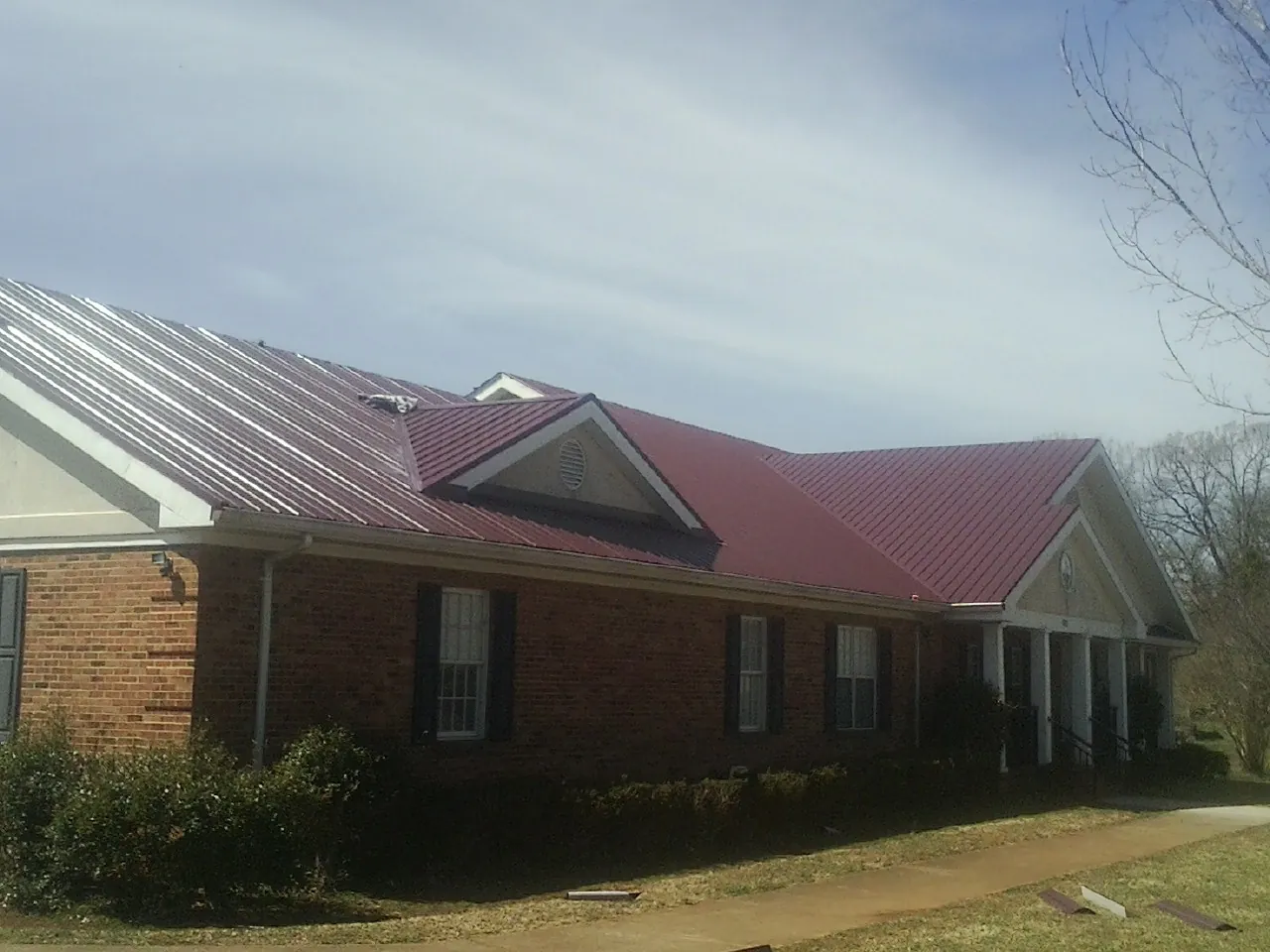 Red metal roof with gabled entries on a long brick building, from a Hail Damage Roof Repair job in Poseyville