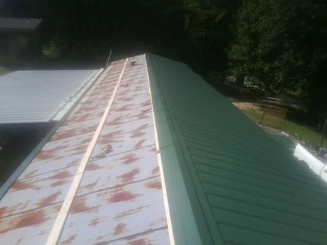 Old rusted panels beside newly installed green metal roofing — Wind Damage Roof Repair by Roofing Brothers in Poseyville
