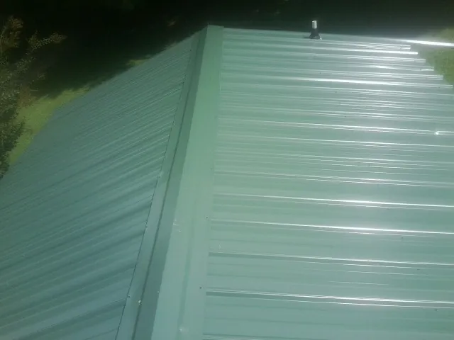 New green metal panels meeting at the ridge of a roof — Flat Roof Repair work by our crew in Poseyville