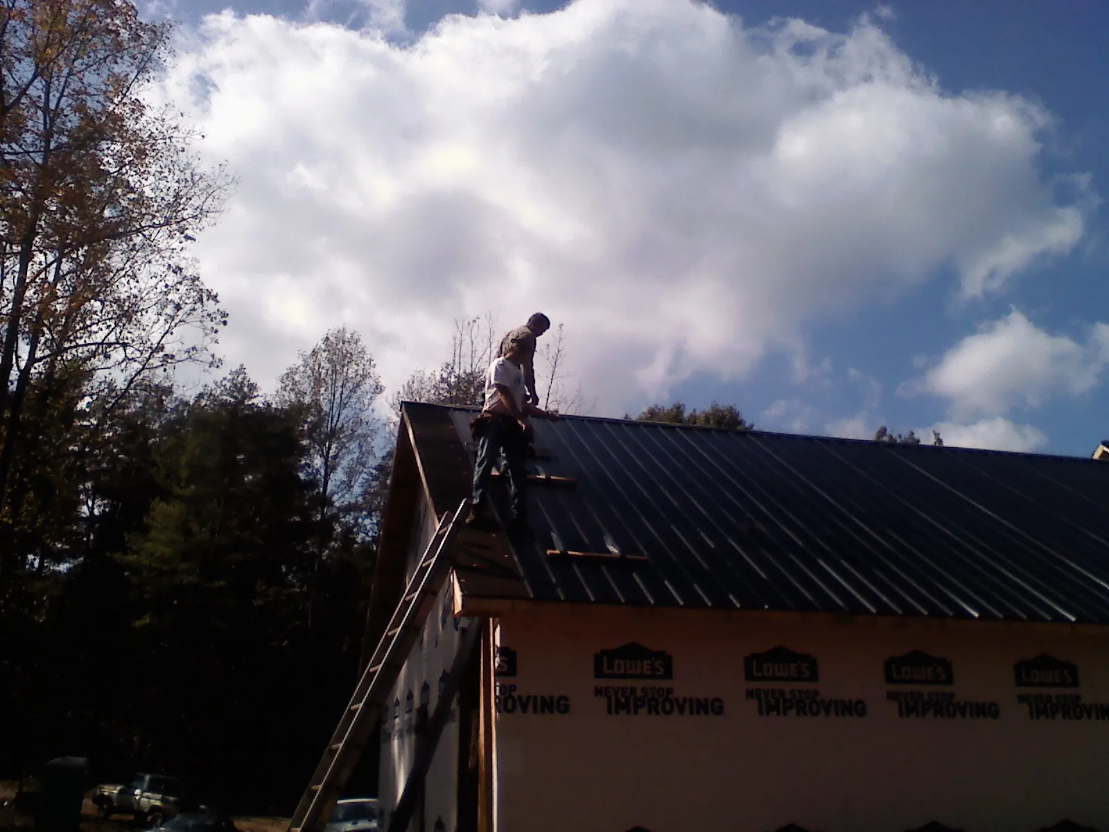 Roofer fastening dark metal panels high against a cloudy sky in Poseyville