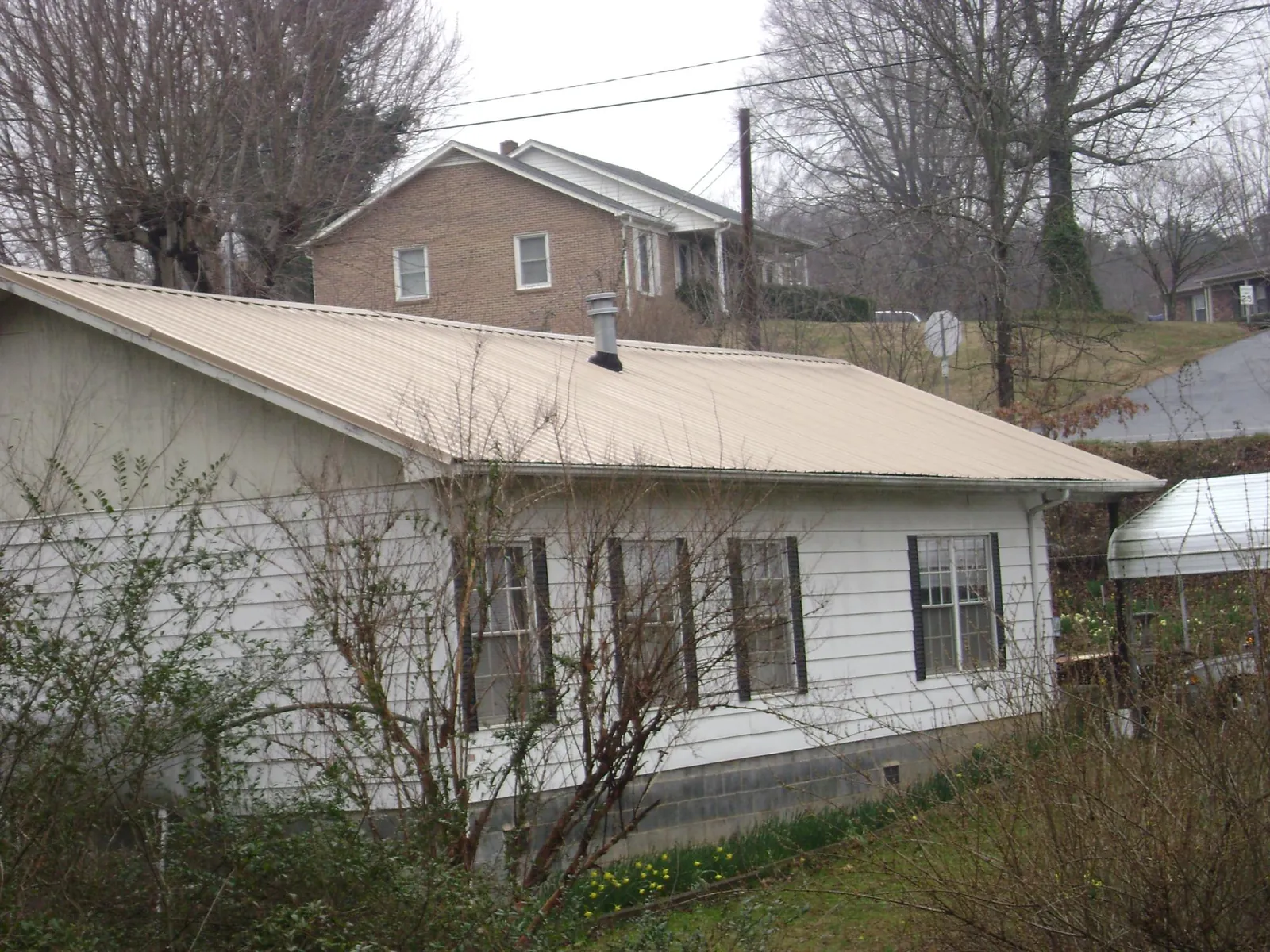 Tan metal roof on a white sided house set into a hillside — Commercial Roofing by Roofing Brothers in Poseyville