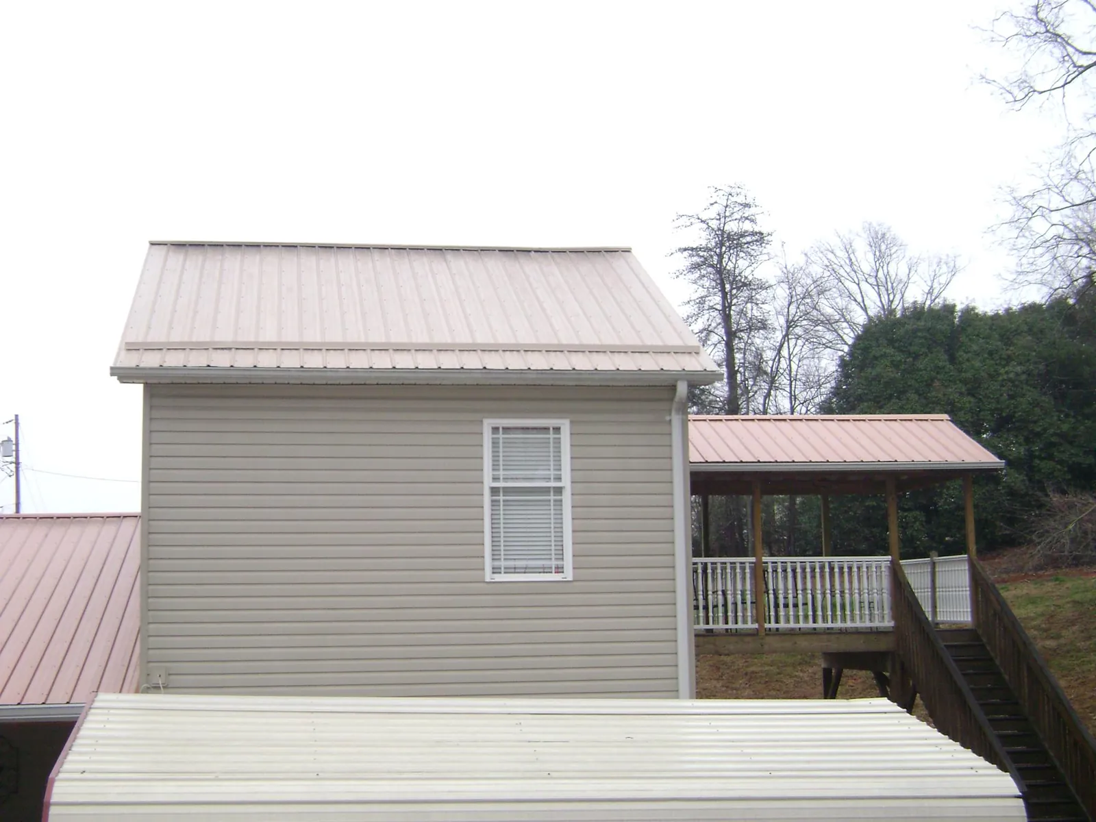 Tan metal roofs on a two story addition and attached porch, from a Roof Replacement job in Poseyville